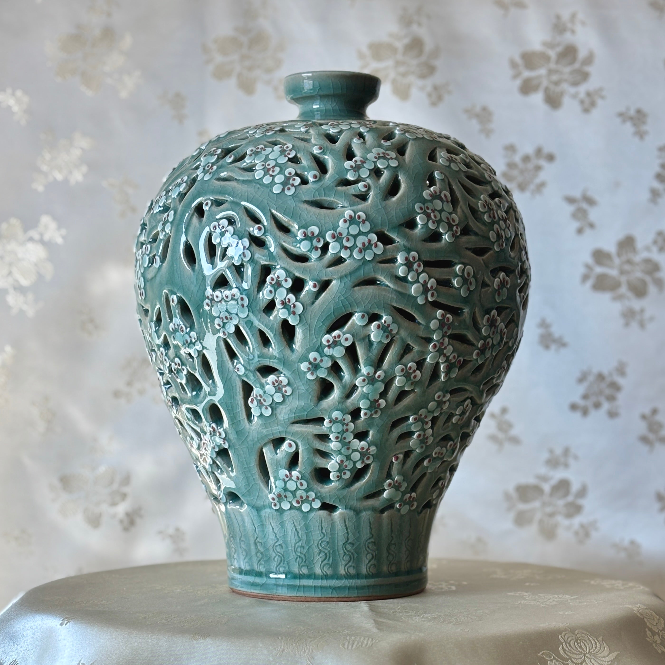 Handmade Korean celadon double-wall openwork vase featuring intricate plum blossom motifs in white and red, showcasing traditional craftsmanship.