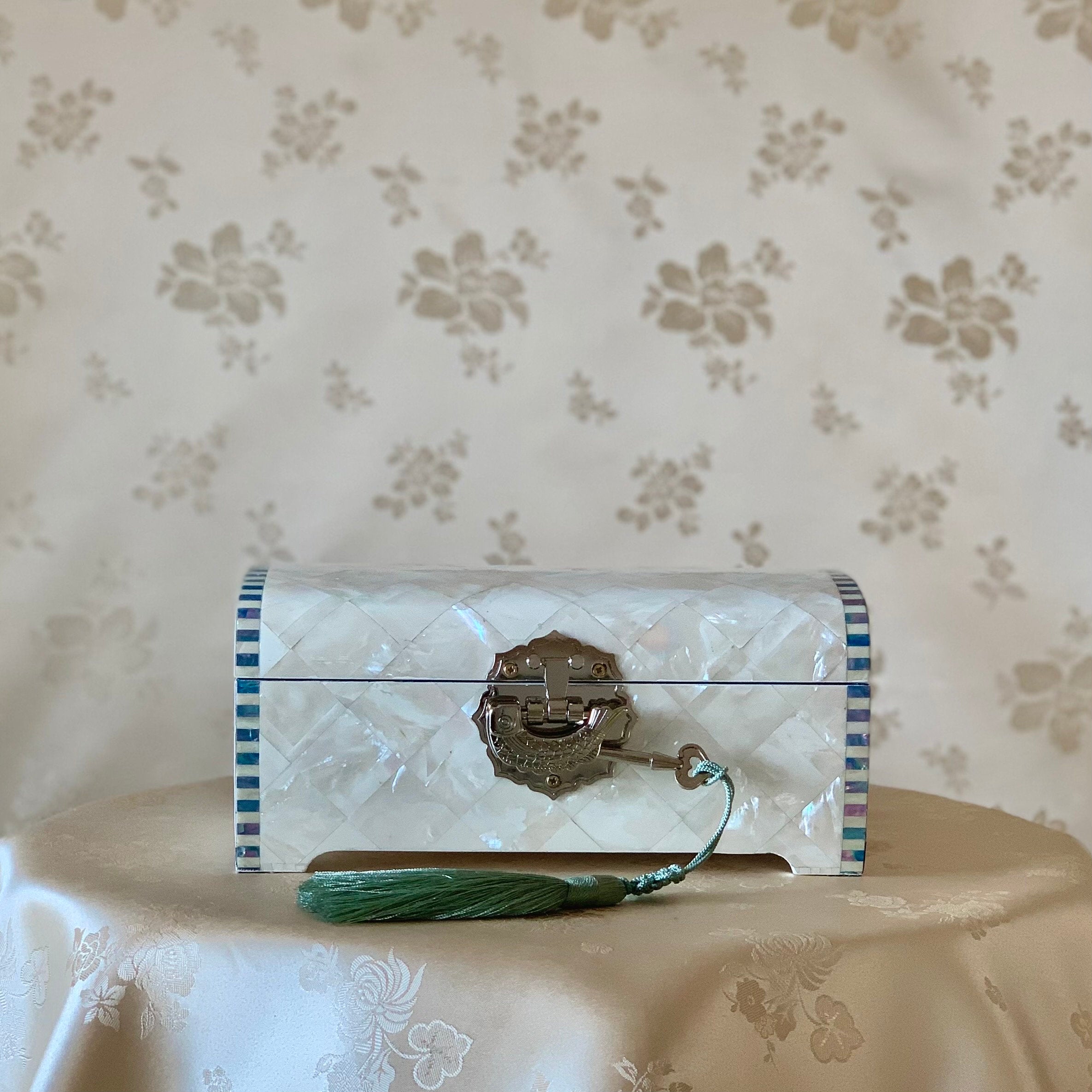 Front view of a handmade Korean white mother of pearl wooden jewelry box with a checkered pattern and a green tassel key.